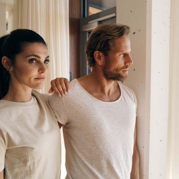 Philosophy Couple in casual beige clothing gazing out a bright window in modern interior